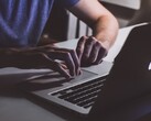 Hände tippen im Halbdunkel auf der Tastatur eines MacBooks, das Apple-Logo leuchtet
