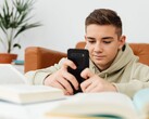 Jugendlicher im Hoodie tippt auf einem Smartphone, davor liegen aufgeschlagene Schulbücher
