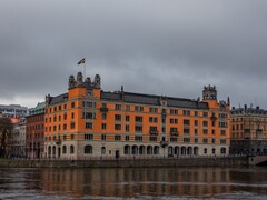 Orangefarbenes Rosenbad-Gebäude mit schwedischer Flagge am Wasser in Stockholm unter bewölktem Himmel